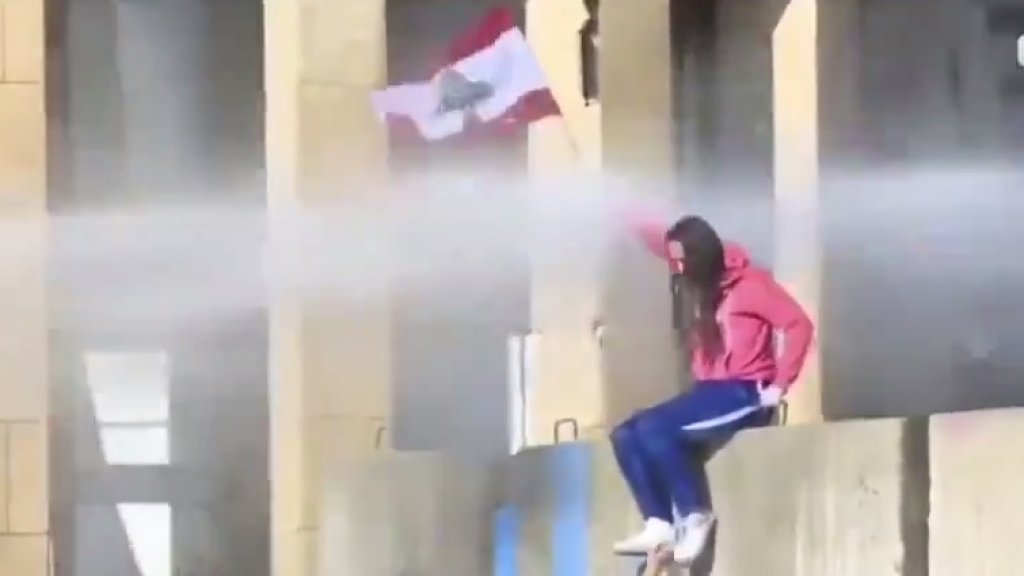 بالفيديو/ فتاة تتسلق الجدار الاسمنتي في وسط بيروت وتجلس رافعة العلم اللبناني رغم خراطيم المياه التي تطلقها القوى الامنية باتجاه المتظاهرين!